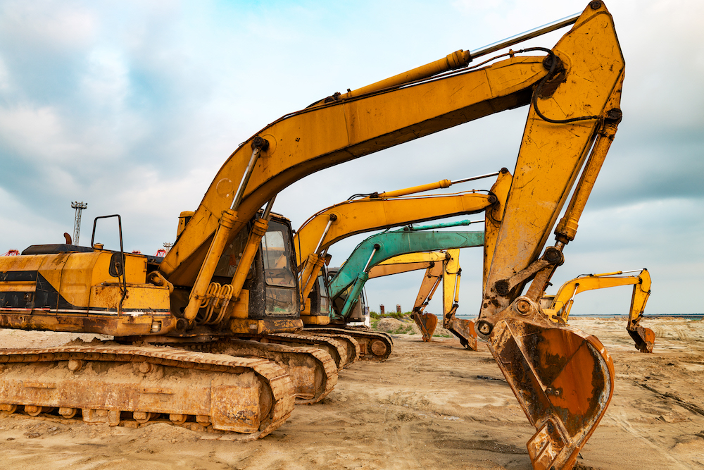 row of yellow and green excavators are lined up in the dirt